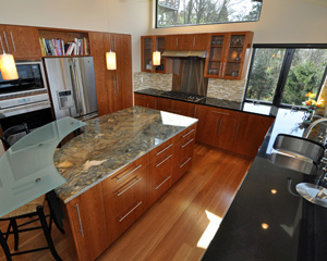 By pushing back the East wall, the kitchen gets a larger footprint.  That allows room for an elegant island with substantial storage and a bar eating area.  Bookmatched cherry cabinets define the room and a stunning track light with Onyx shades supplements the lighting plan.  The Vesuvio Oro slab required careful fabrication, yielding an interesting counter with visual depth