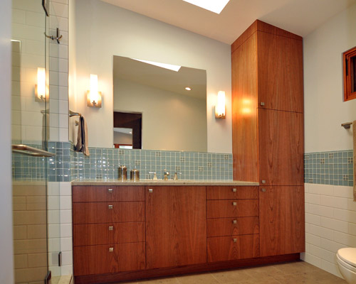 The bath vanity stays in the same spot but the toilet moves, accommodating custom cherry cabinets with flush doors.  One of the owners designed the tile pattern that makes up the backsplash and extends through the niche in the shower.  Jura grey limestone is used for the counter and for the floor tile