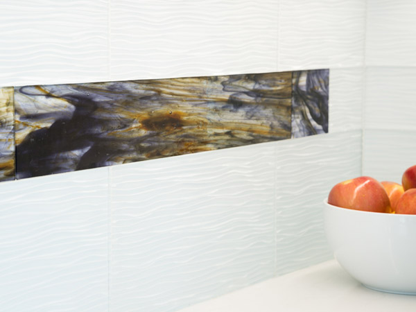 The backsplash is a custom glass tile from Pental called Midnight 4x24 and is best viewed in person to see the subtle colors and their play with the cabinets and the deep blue of the water just outside the window.  It nestles in between lighter-colored Teqa Blanco tile from Statements