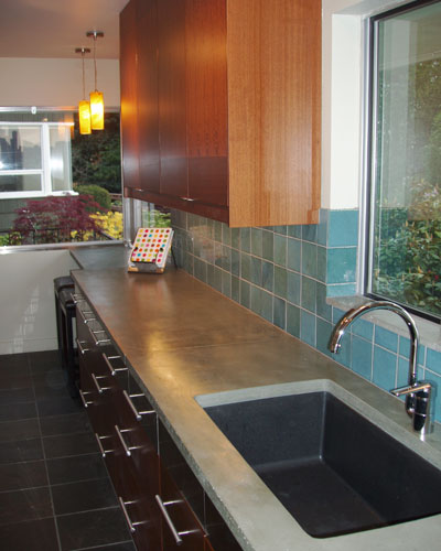 It's a whole new era for this 50s rambler kitchen.  Not a single wall moved, but this transformation is total.  Modern cabinets, a green countertop from Squak Mountain Stone, and cool recycled glass tiles bring this kitchen remodel into the new century. Modern galley kitchen